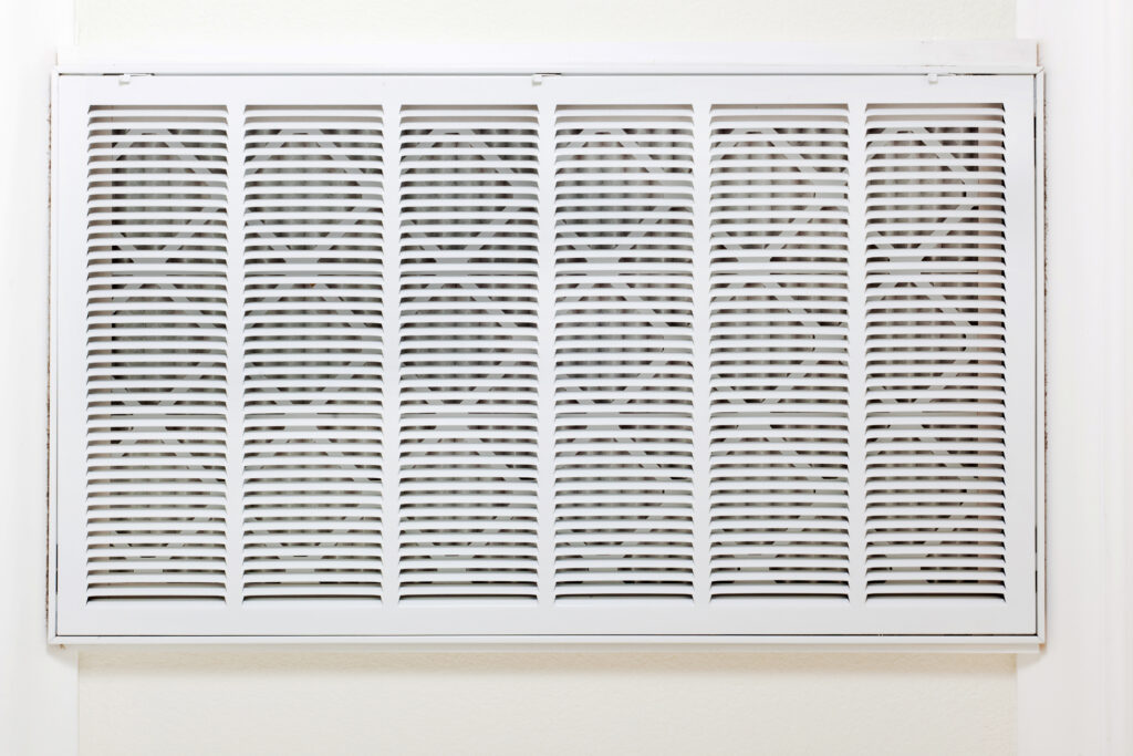 A white metal air vent cover with horizontal and vertical slats mounted on a light-colored wall.