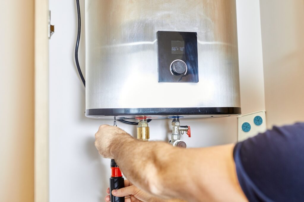 Technician using a screwdriver to adjust or repair a wall-mounted electric water heater with a digital display.